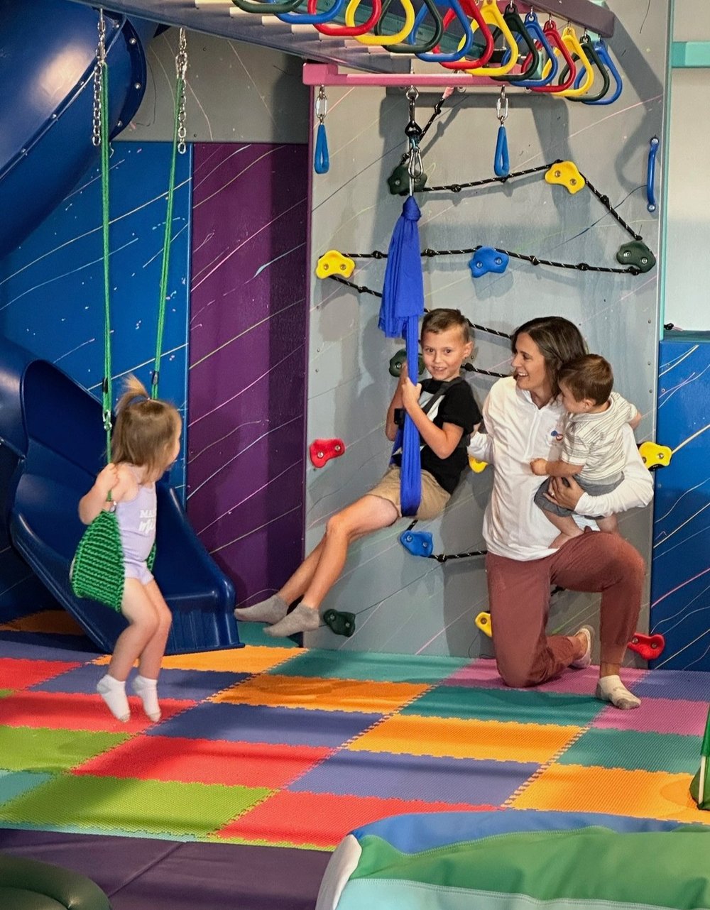 Children and a caregiver enjoying the swings and climbing area at The Grove