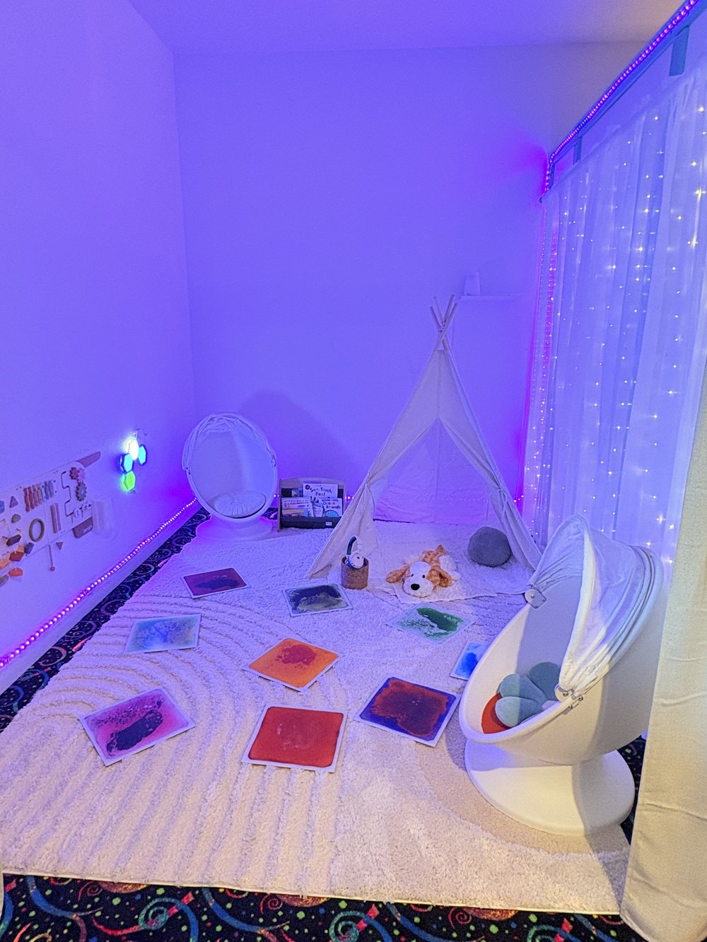 Sensory room with soft lighting, hanging chairs, books and a play tent