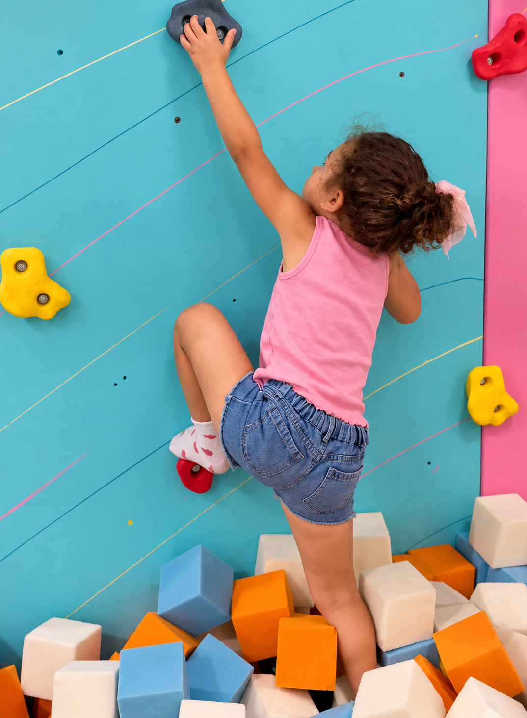 A child climbing the colorful climbing wall above the foam pit at The Grove