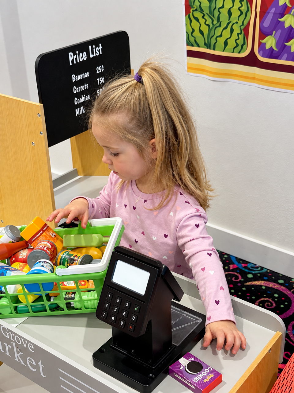 A child exploring pretend groceries and a toy cash register at The Grove